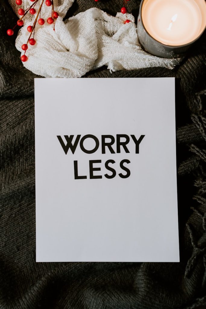 A piece of paper with the text "WORRY LESS" is placed on a dark fabric with a lit candle and red berries nearby.