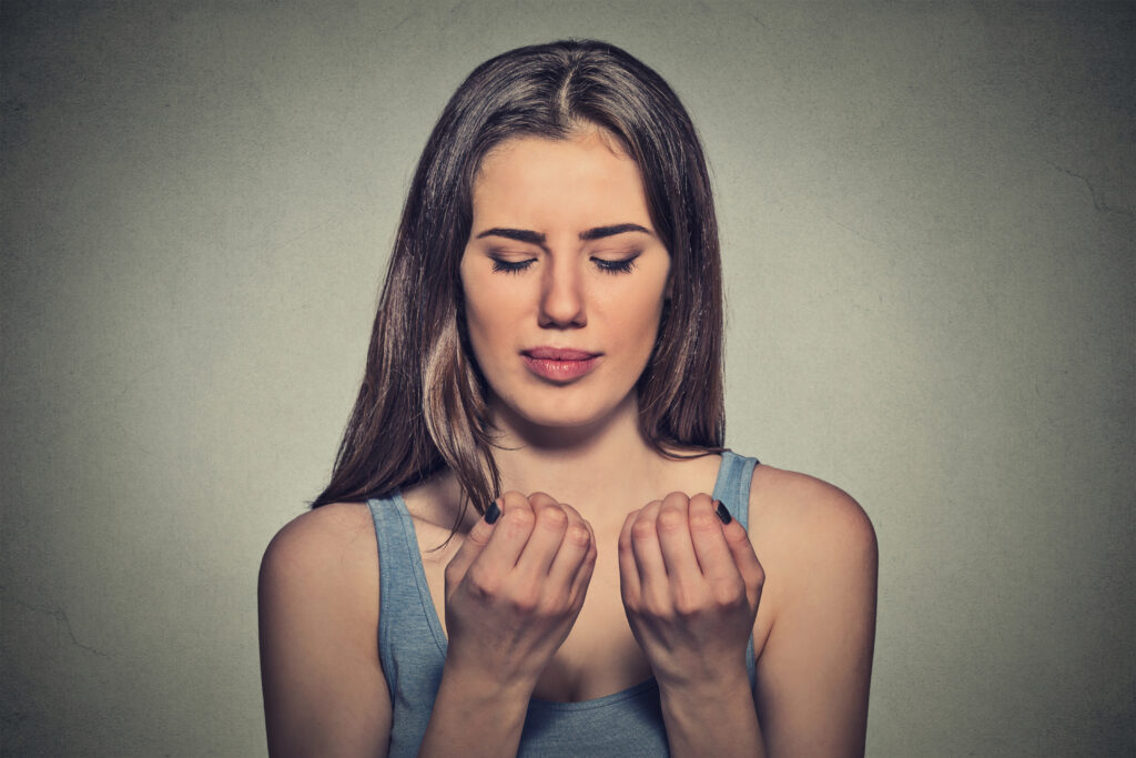 A woman with long hair, wearing a blue tank top, looks at her hands with a focused expression against a textured background.